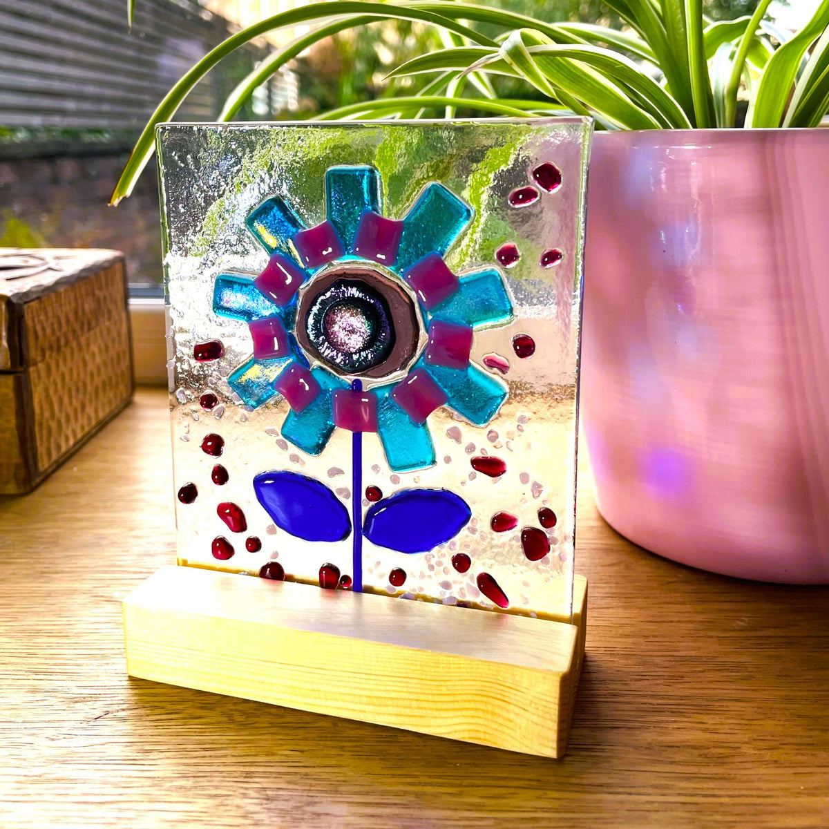 Angled view of colourful fused glass flower art in pine base