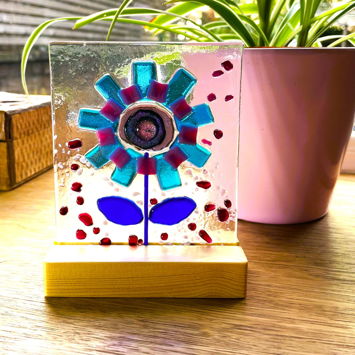 Freestanding fused glass flower panel glowing in window light