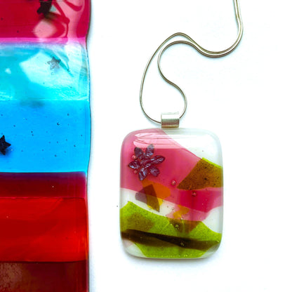 Close-up of a colourful fused glass pendant with pink, purple, green and copper details