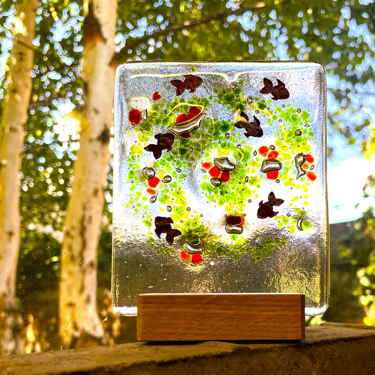 Fish fused-glass suncatcher with wooden base displayed outdoors in sunlight