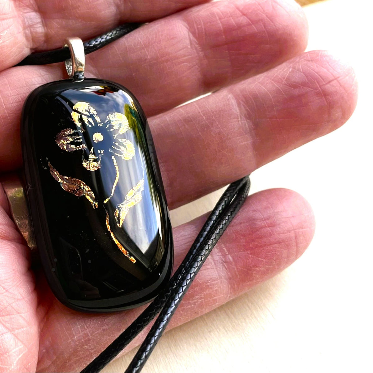 Back of a glossy black fused glass pendant showing the silver-plated bail and black cord necklace