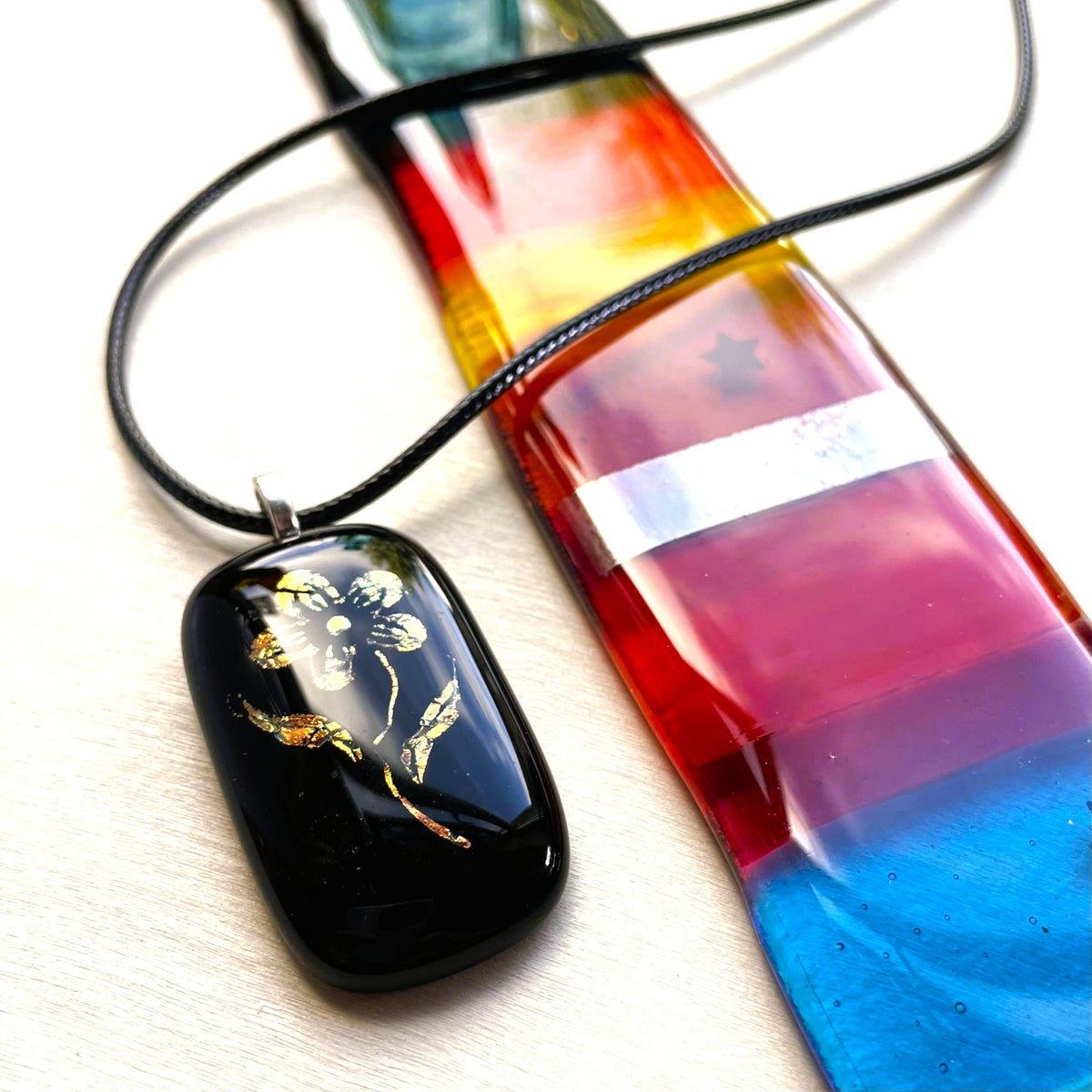 Vintage-inspired black glass pendant with shifting gold and copper dichroic colour displayed beside colourful glass