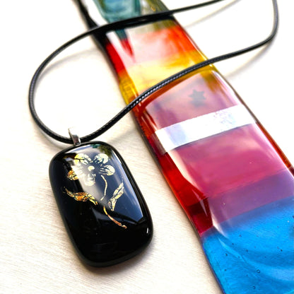 Vintage-inspired black glass pendant with shifting gold and copper dichroic colour displayed beside colourful glass