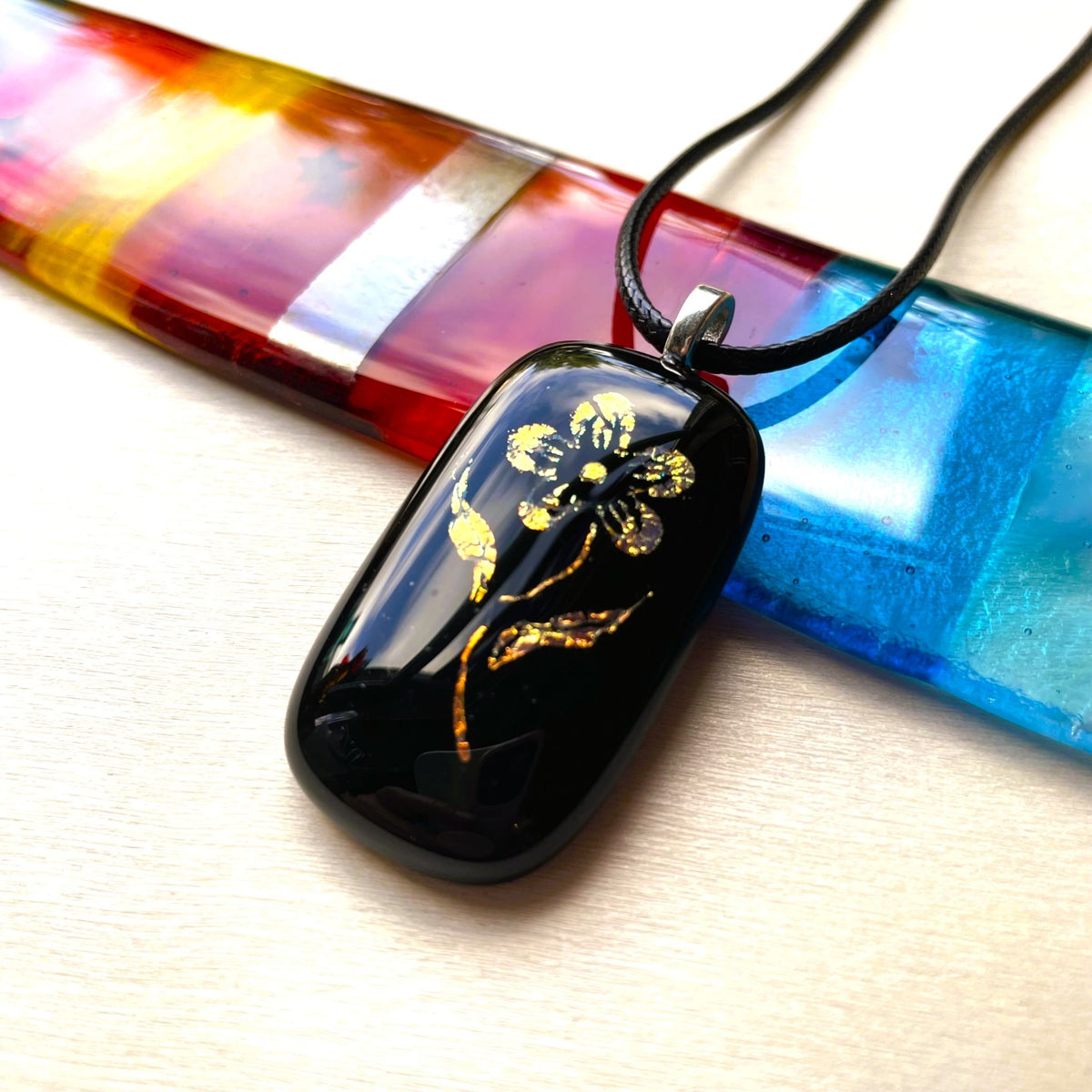 Close-up of a glossy black fused glass pendant with gold and copper dichroic floral details