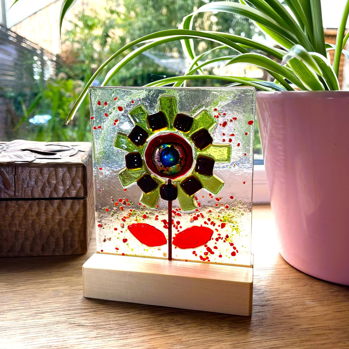 Handmade green and red fused glass flower panel on a sunny windowsill