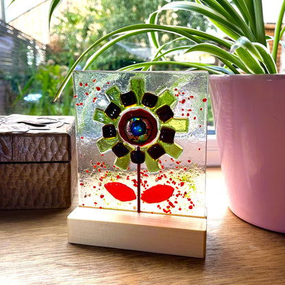 Handmade green and red fused glass flower panel on a sunny windowsill