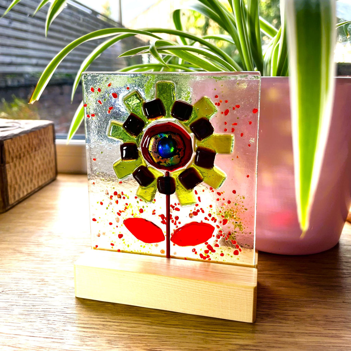 Freestanding green and deep red glass flower panel glowing in sunlight