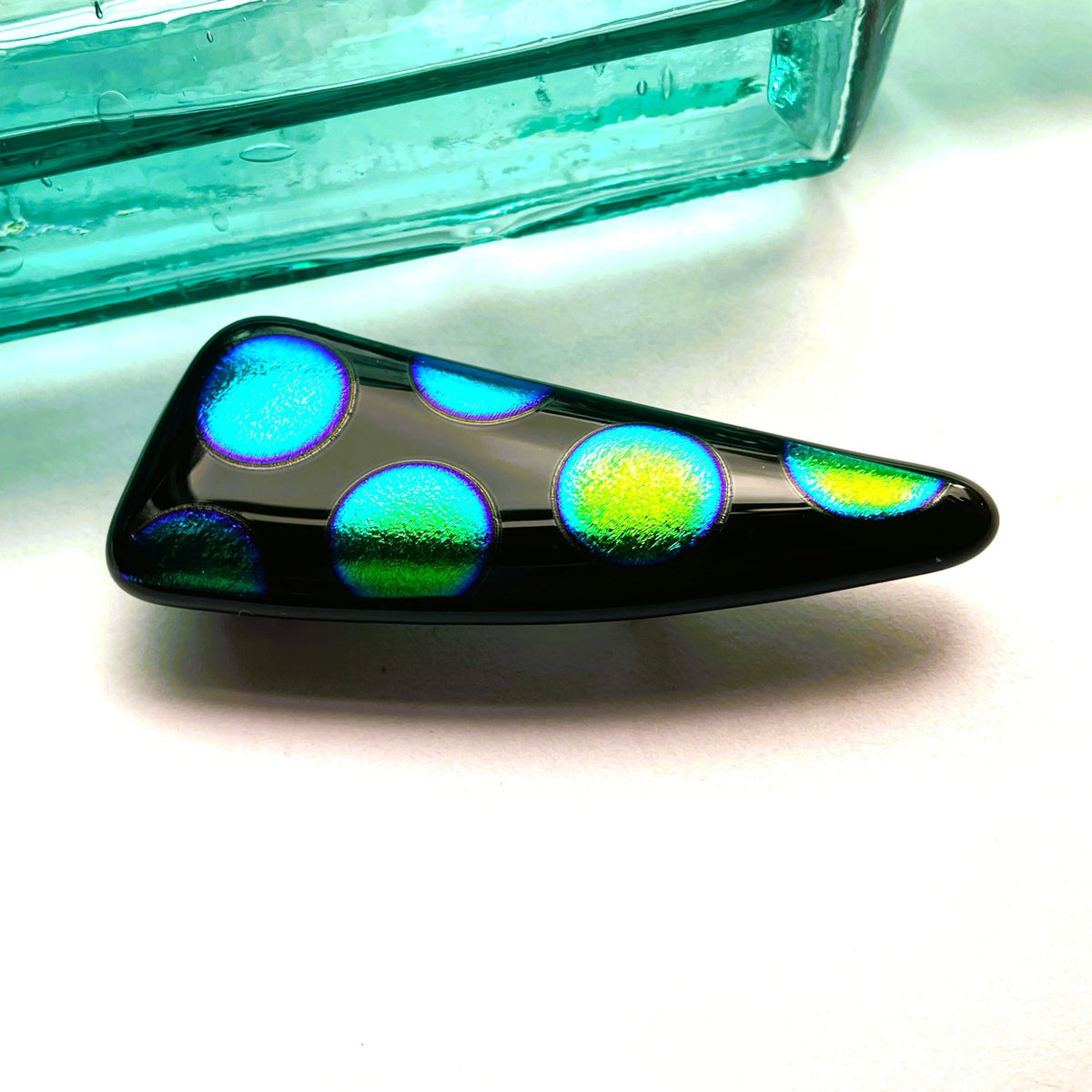 Close view of glossy black fused glass with textured blue, green and gold dichroic spots