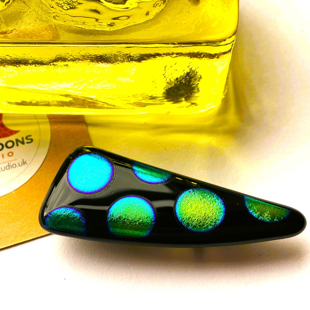 Long black fused glass brooch with peacock-coloured dichroic spots in blue, green and gold