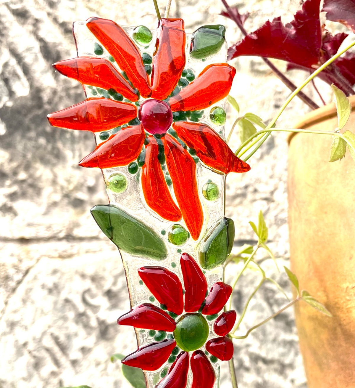 Close-up of a bright red fused-glass flower plant stake with green leaves and glass nuggets