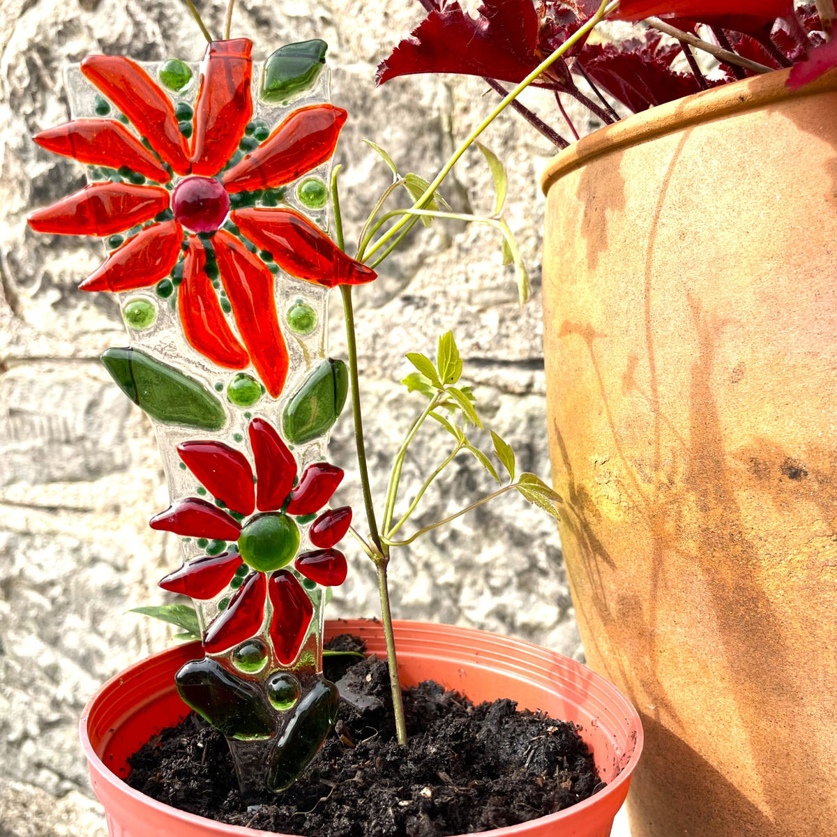 Full view of a handmade red fused-glass flower plant stake with green leaves