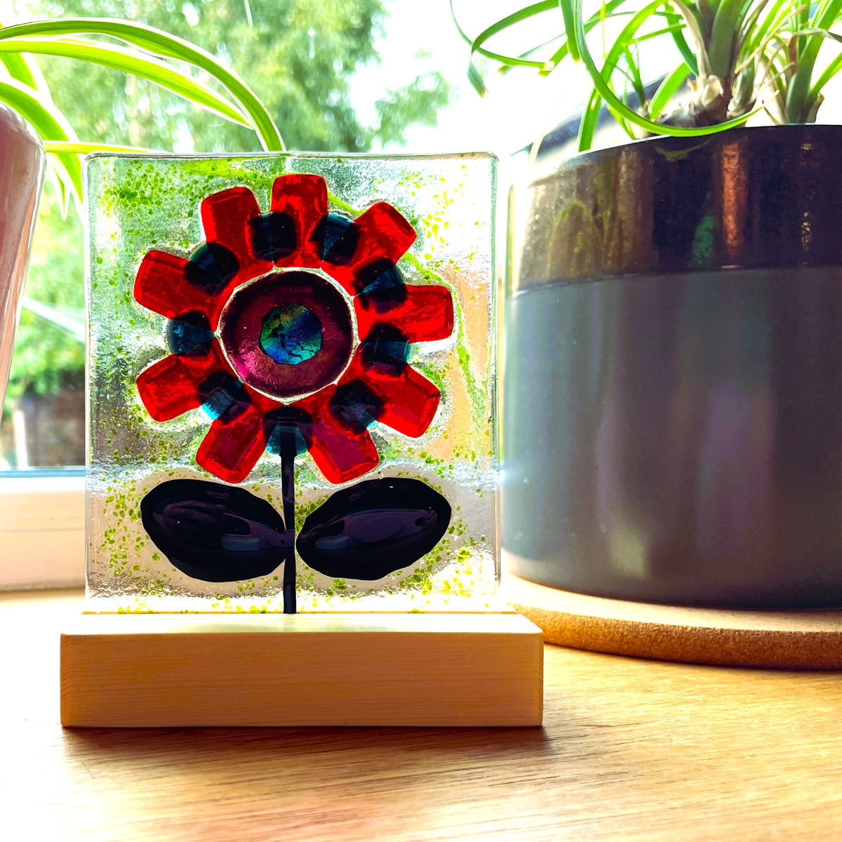 Red fused glass flower panel glowing in sunlight on a windowsill