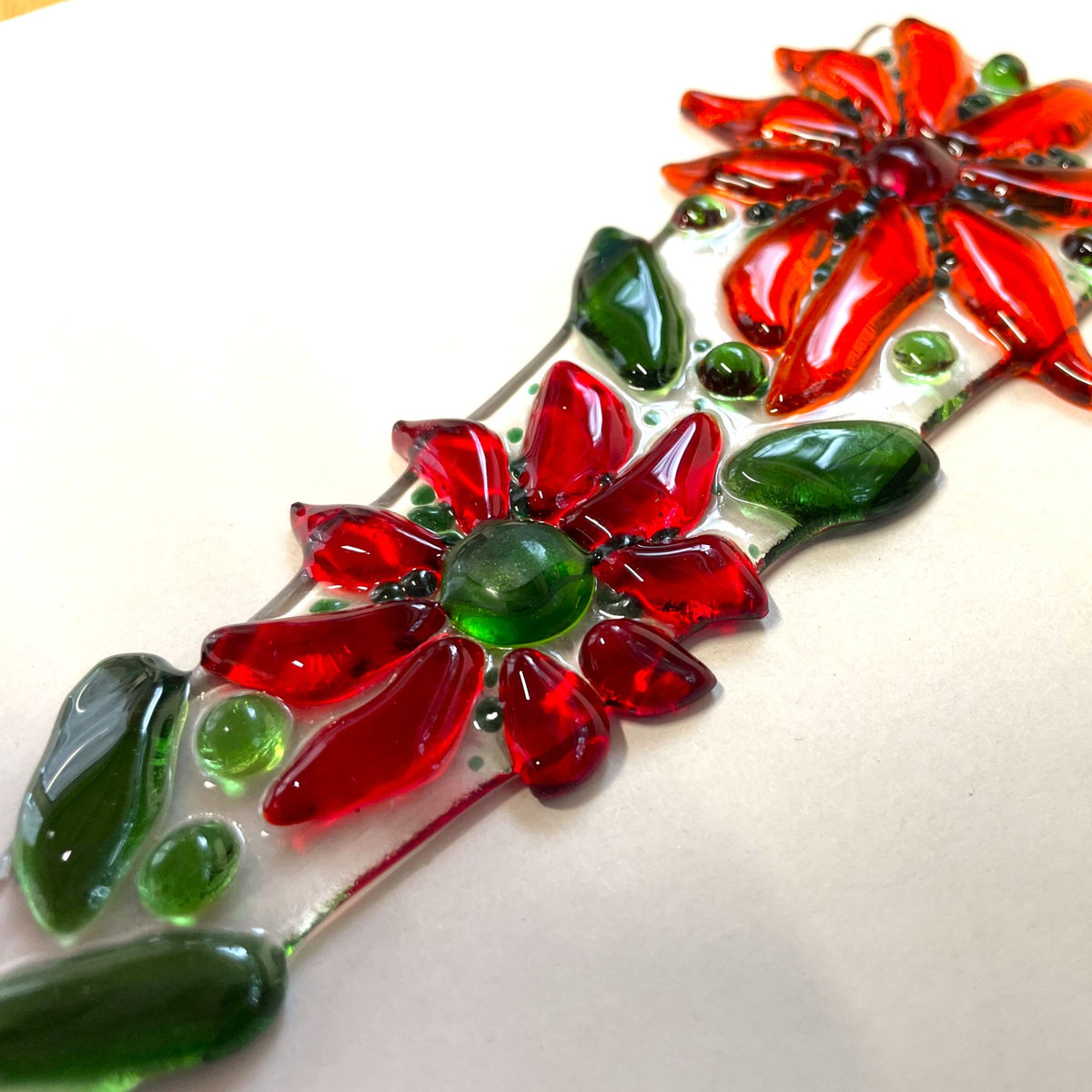 Detail of red fused-glass flowers and green leaves on a plant stake