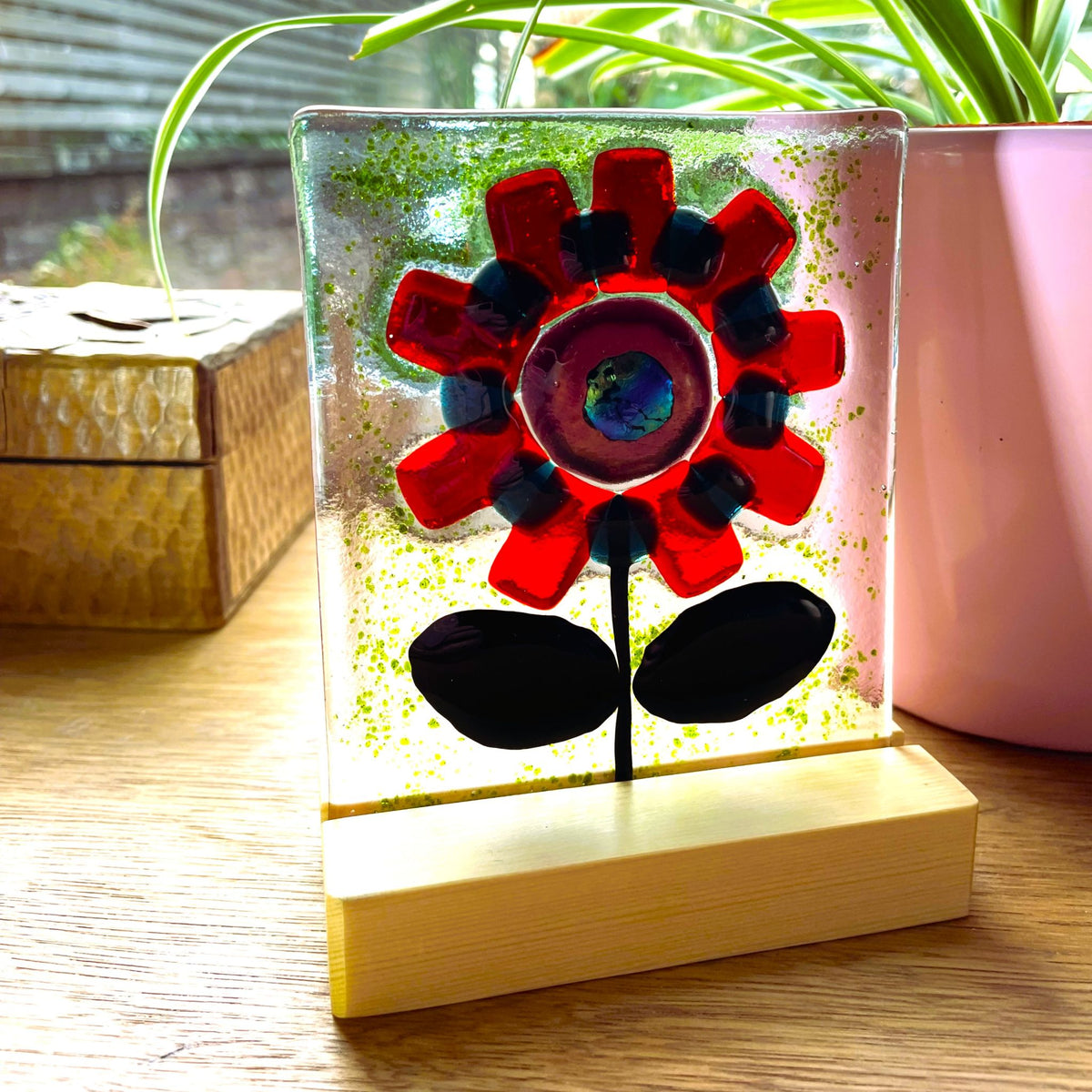 Angled view of a red fused glass flower suncatcher standing in a pine base