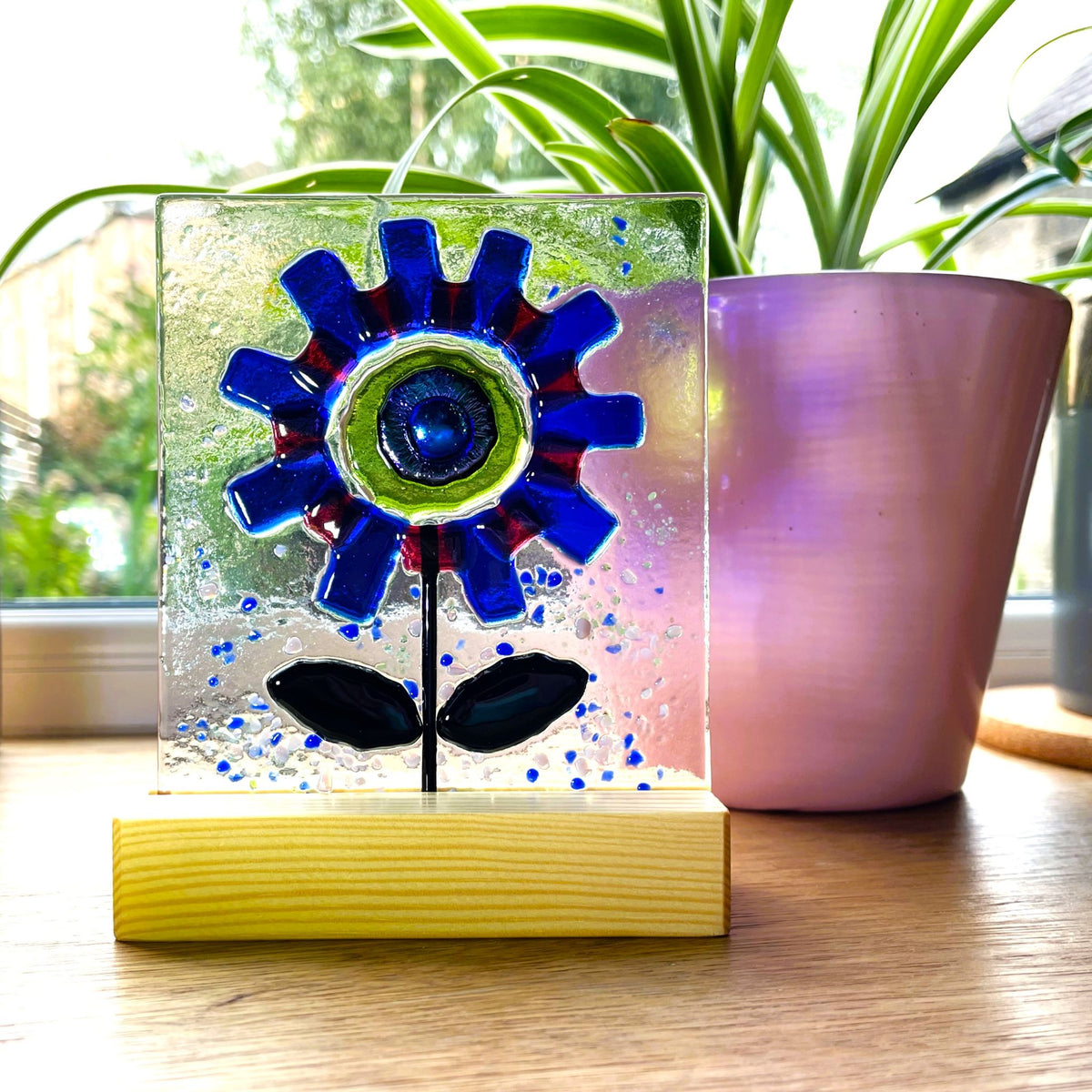 Blue glass flower suncatcher with vivid green centre on a windowsill