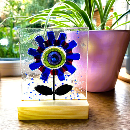 Cobalt-blue fused glass flower with red accents and dark leaves