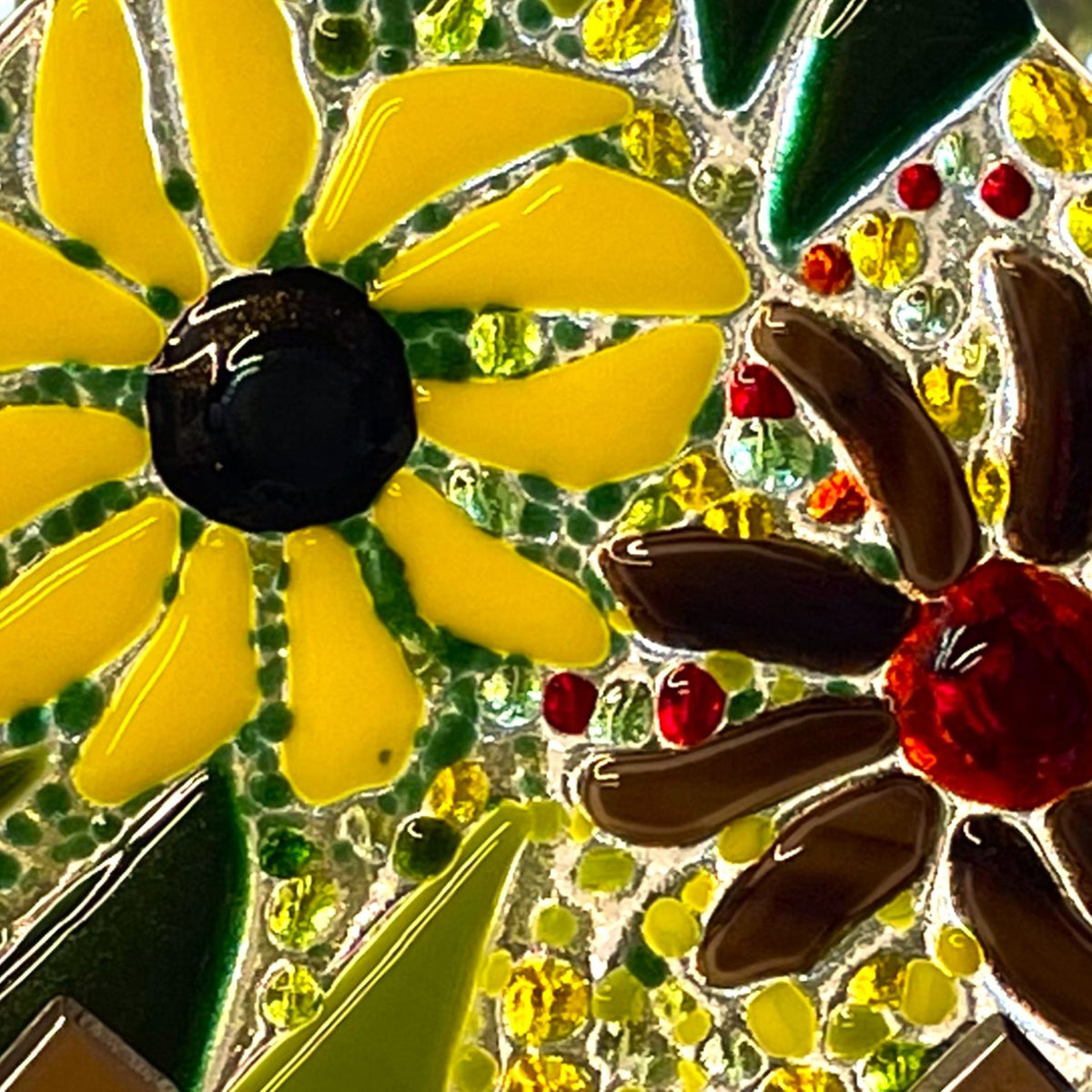 Close-up of yellow and brown fused-glass flowers with green leaves and sparkle