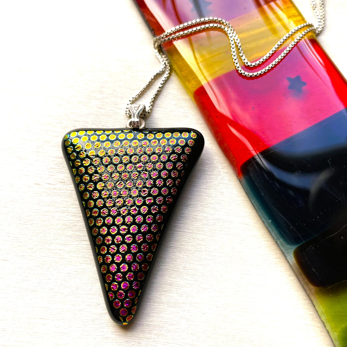 Back of a black triangular fused glass pendant showing its glossy textured finish