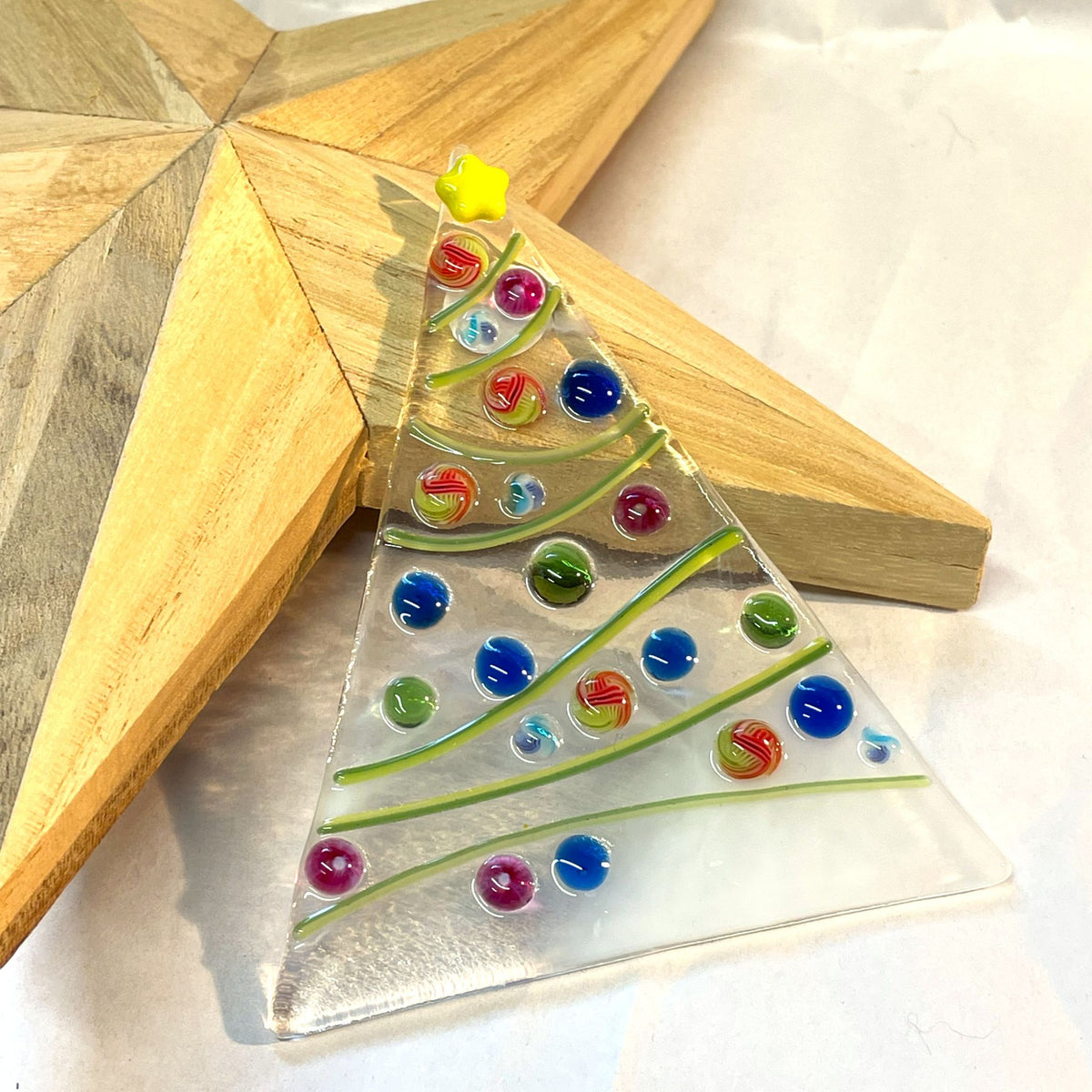 Close-up of white and clear streaky fused glass Christmas tree with green tinsel and colourful glass baubles