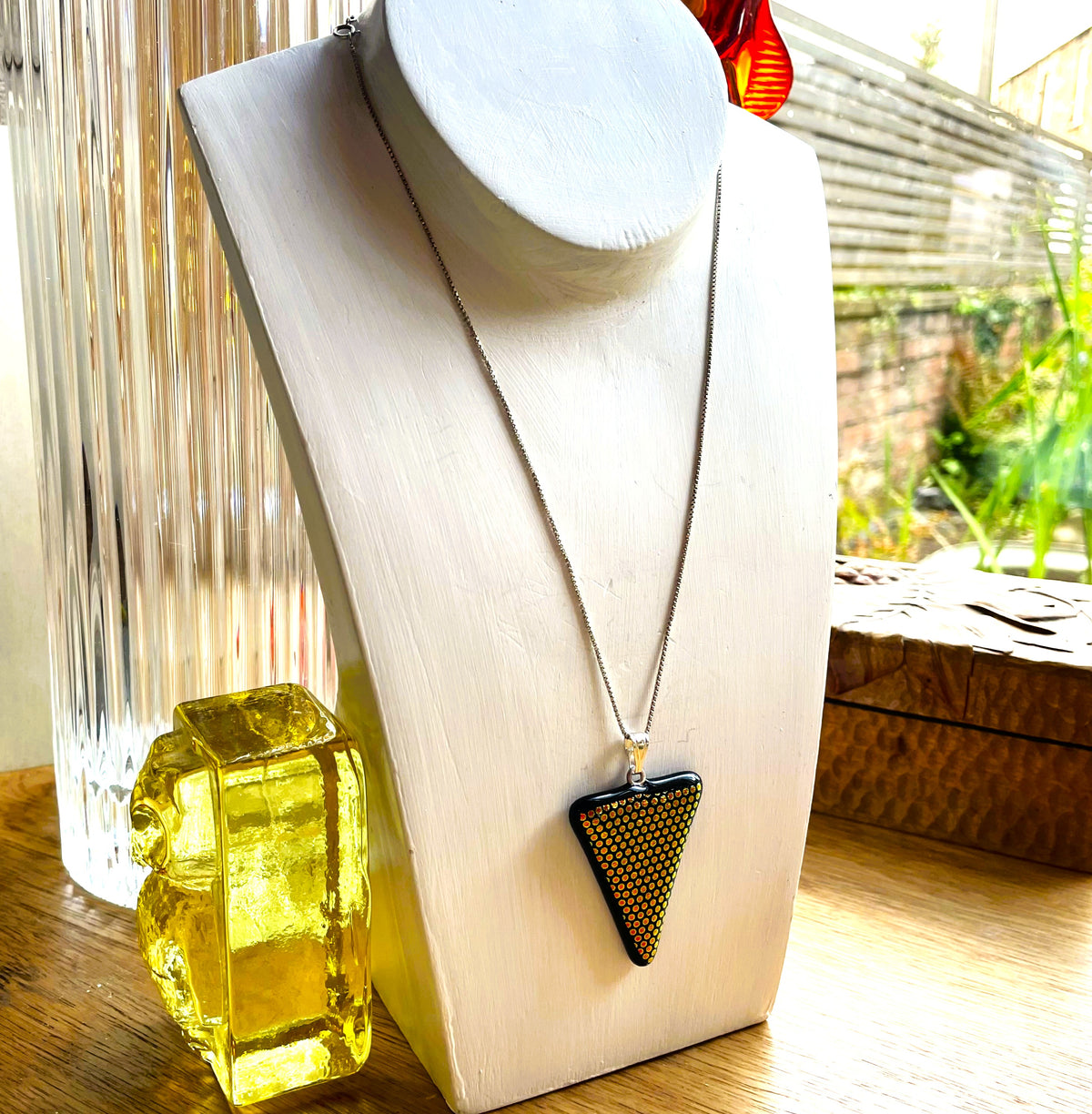 Black triangular dichroic glass pendant held in a hand to show its size