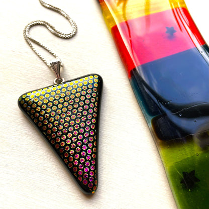 Close-up of a black triangular pendant with yellow, gold and pink dichroic glass dots