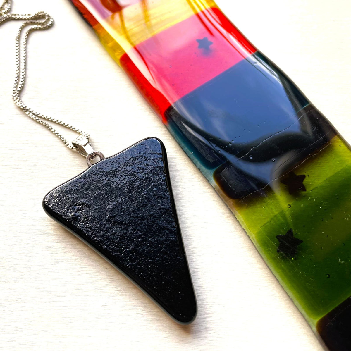 Black triangle dichroic glass pendant displayed on a jewellery bust with its sterling silver chain