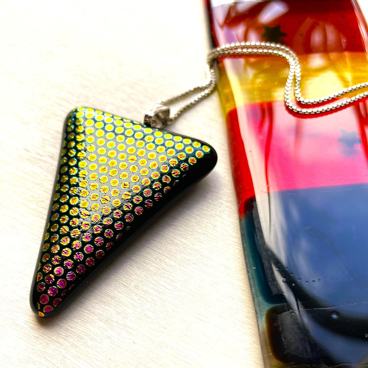 Black triangular fused glass pendant covered with tiny glowing dichroic dots on a sterling silver chain